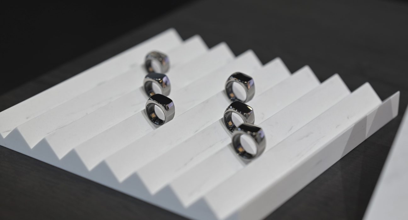 Primer plano de un anillo inteligente plateado Mentoring 2 en la mano de una persona trabajando, con una interfaz digital de batería emocional al fondo.