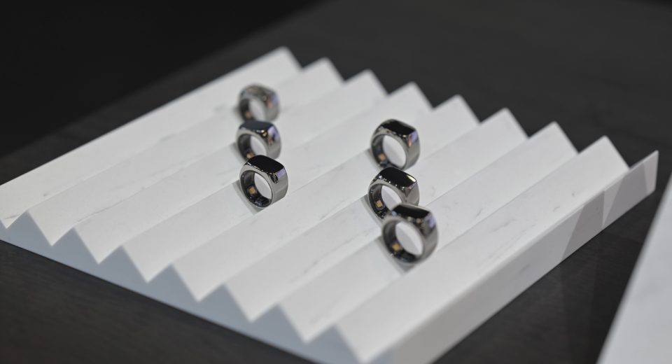 Primer plano de un anillo inteligente plateado Mentoring 2 en la mano de una persona trabajando, con una interfaz digital de batería emocional al fondo.