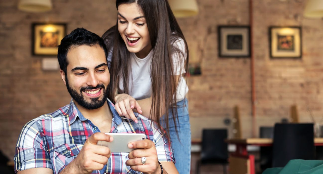 Mano sosteniendo un smartphone del cual emergen elementos de viaje como un avión y palmeras, junto a logos de PayPal y Despegar, sobre un fondo tecnológico vibrante.
