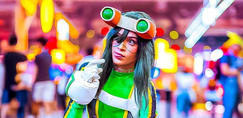 Cosplayer trabajando detalladamente en una armadura futurista dentro de un taller lleno de herramientas y bocetos, con el logo de CCXP México de fondo.